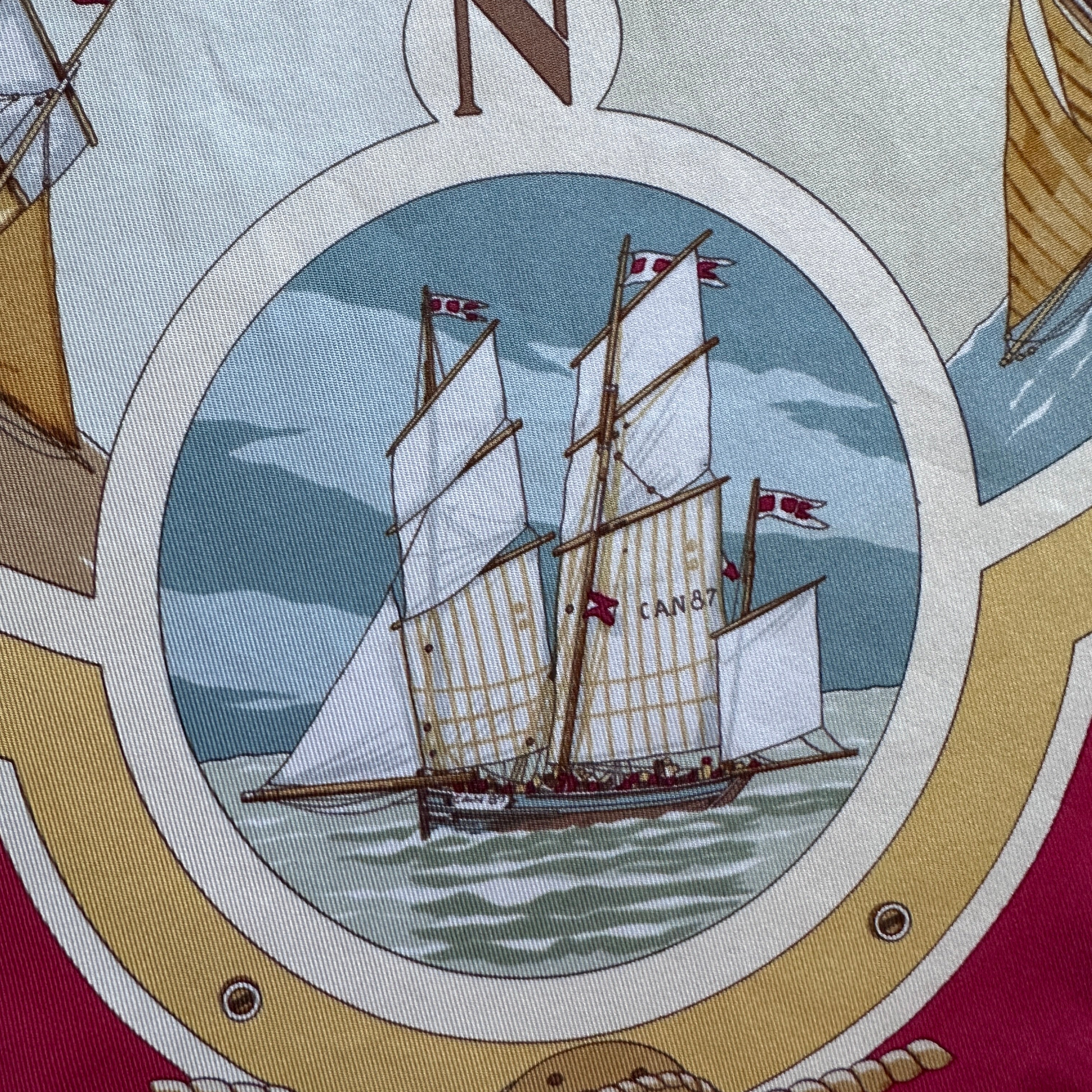 Zoom sur un deux-mâts fines voiles blanches dans un médaillon.