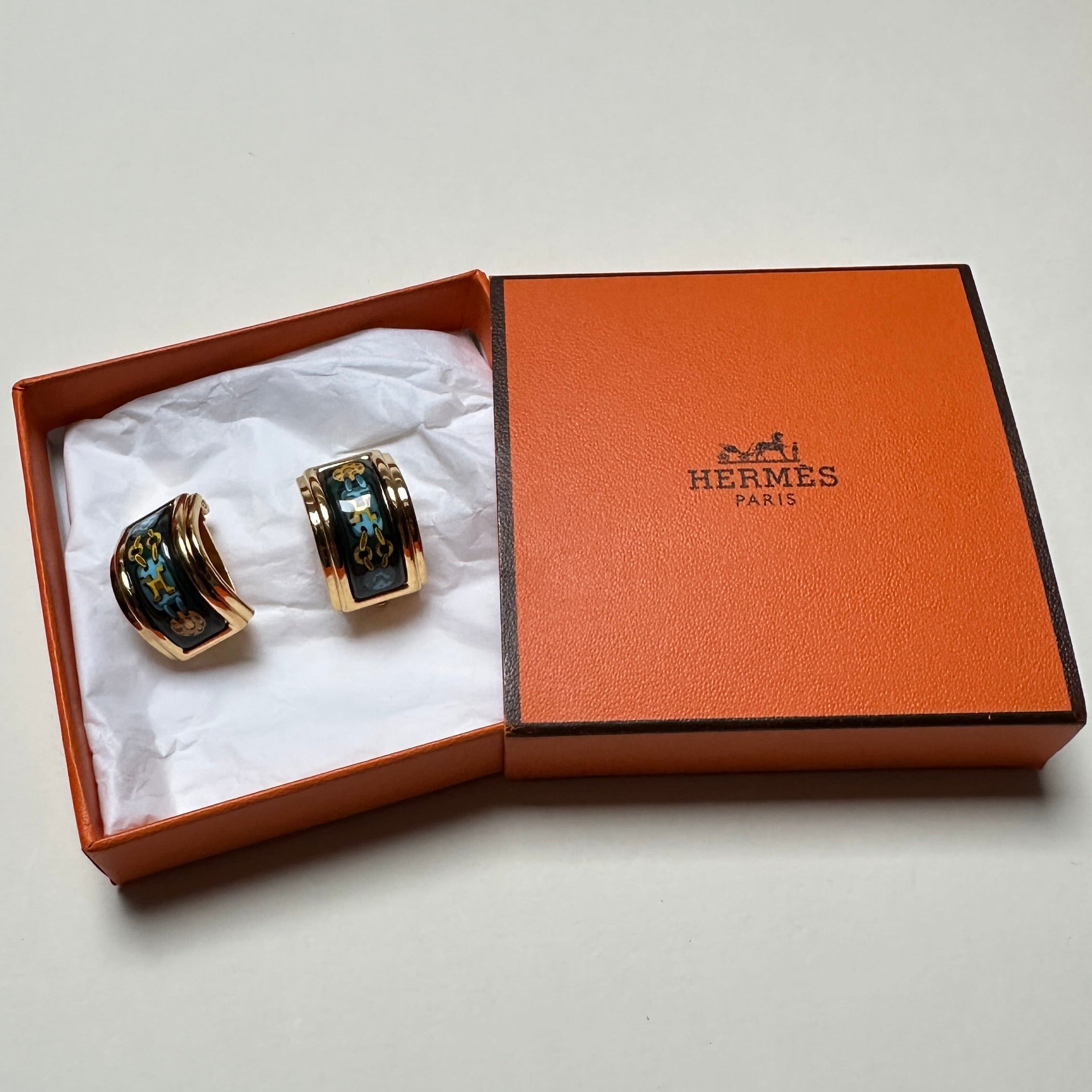 Paire de clips d'oreilles Hermès vintage en émail vert profond et or, présentés dans leur boîte orange d'origine.