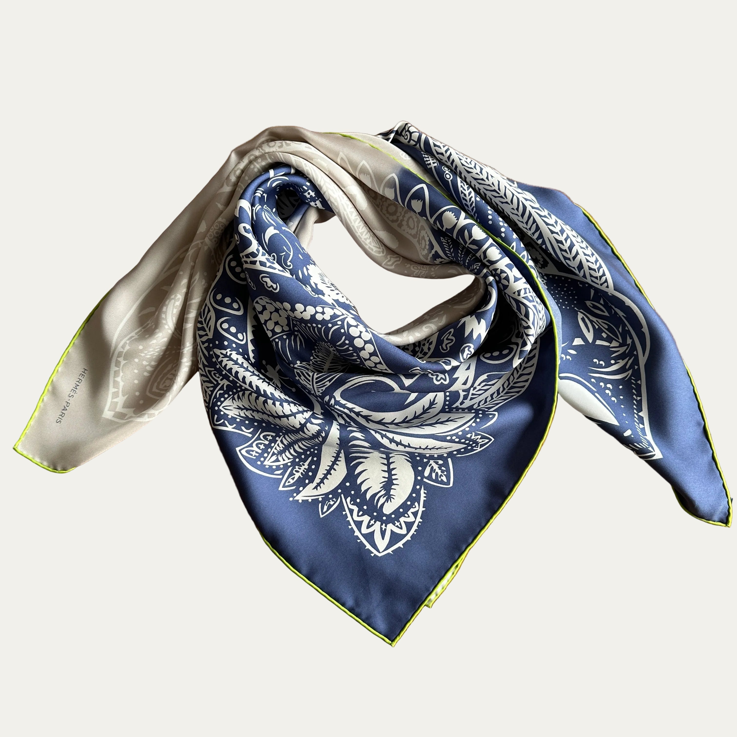 Carré Hermès bicolore plié et noué, illustrant le rendu des couleurs bleu, gris et du liseré vert anis lorsqu'il est porté.