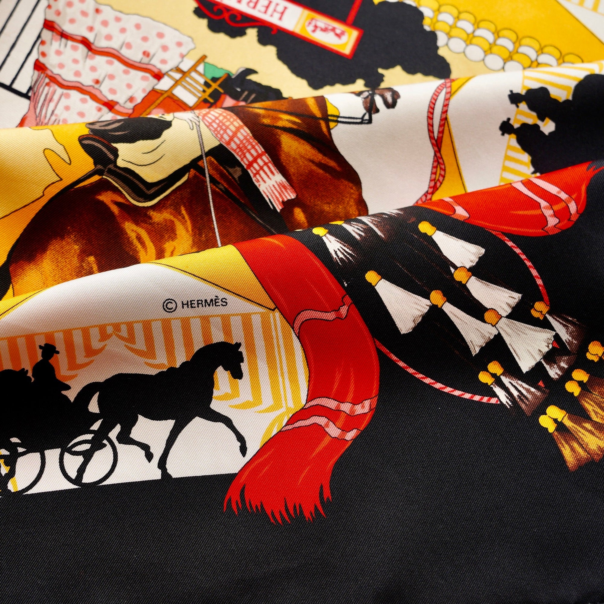 Foulard Hermès Feria de Sevilla plié, mettant en avant le contraste entre le noir, le rouge et l'ocre.