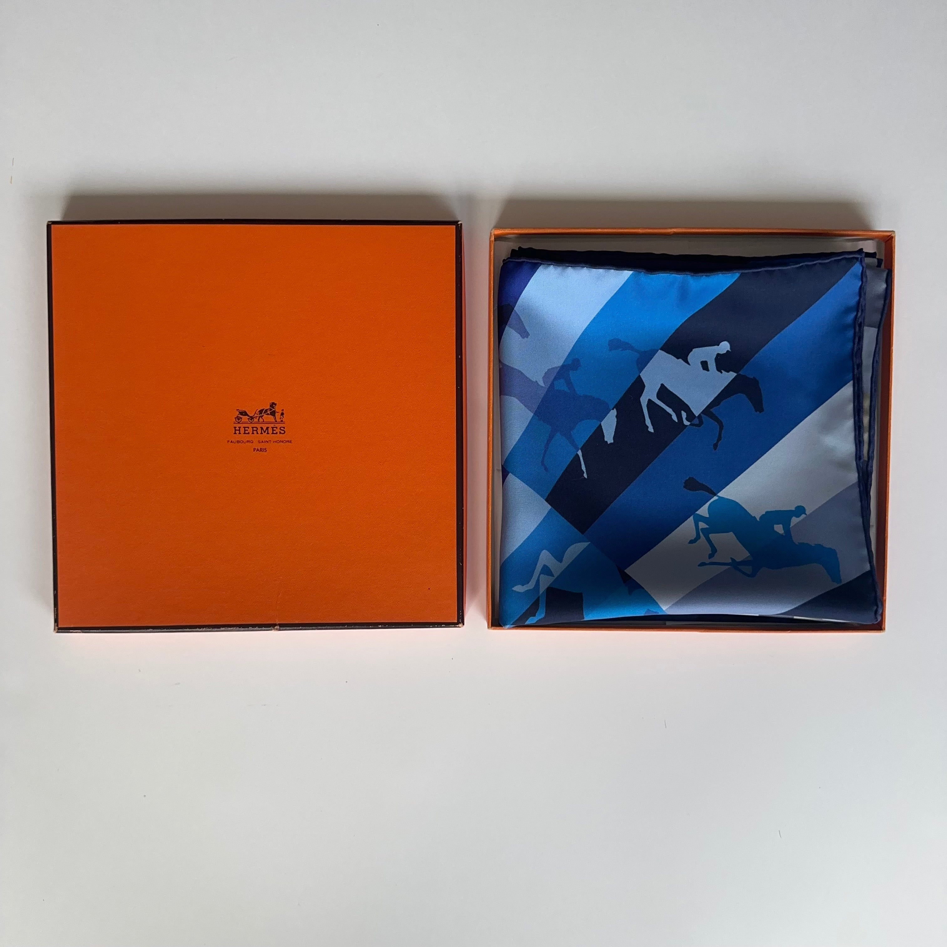 Le carré Hermès Galop Chromatique bleu soigneusement plié et présenté à l'intérieur de sa boîte orange d'origine avec papier de soie.