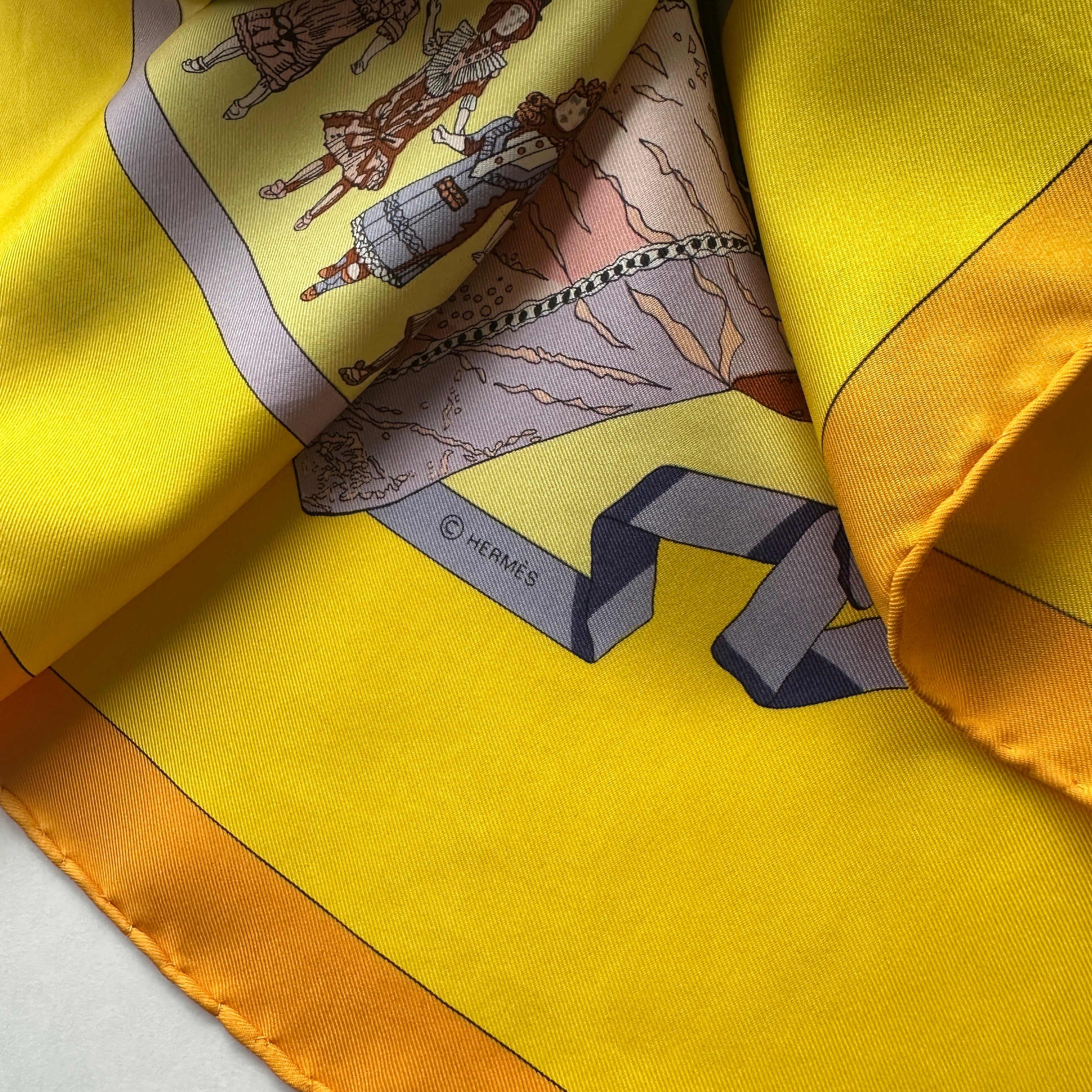 Symbole © HERMÈS imprimé sur un ruban gris, détail de la texture de la soie twill jaune.