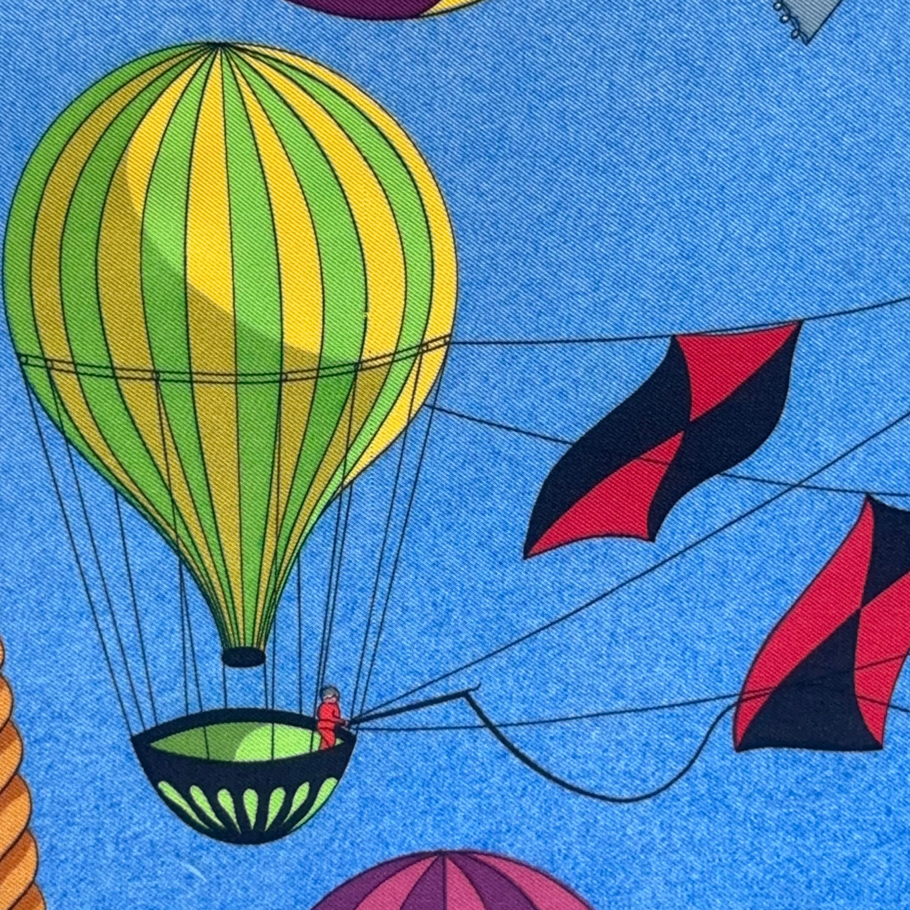 Détail d'une montgolfière verte et jaune rayée avec nacelle noire et cerfs-volants rouges en arrière-plan.