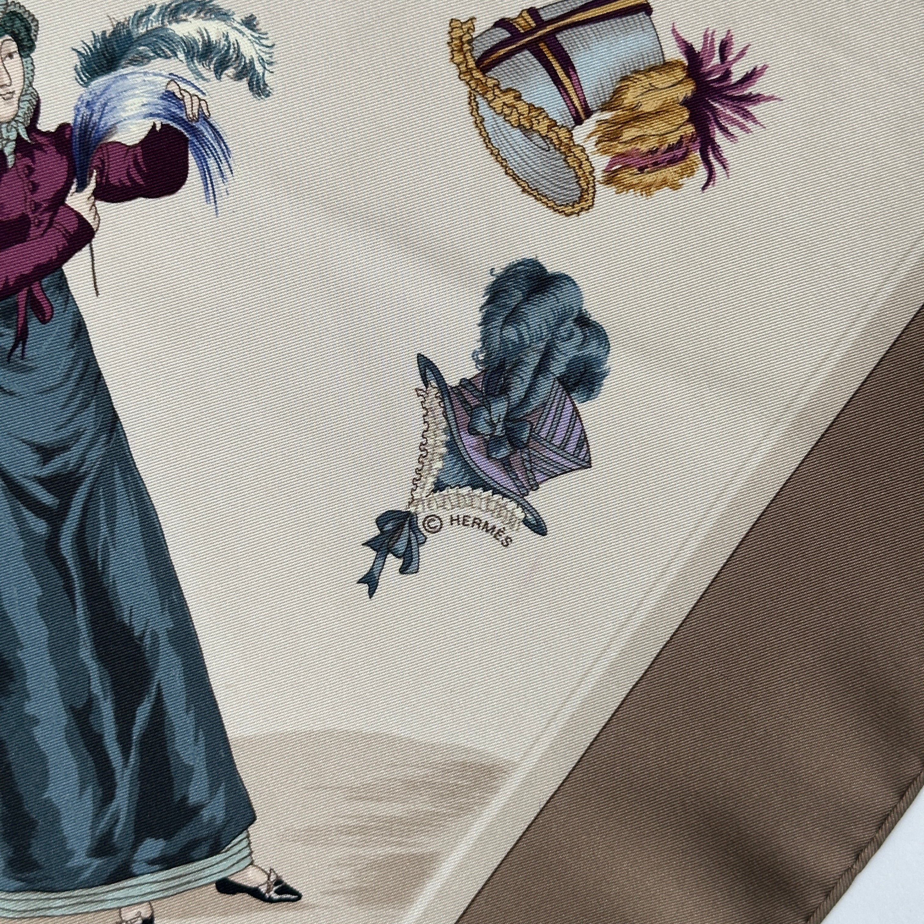 Petit logo © HERMÈS imprimé discrètement sous un chapeau à plumes bleues.