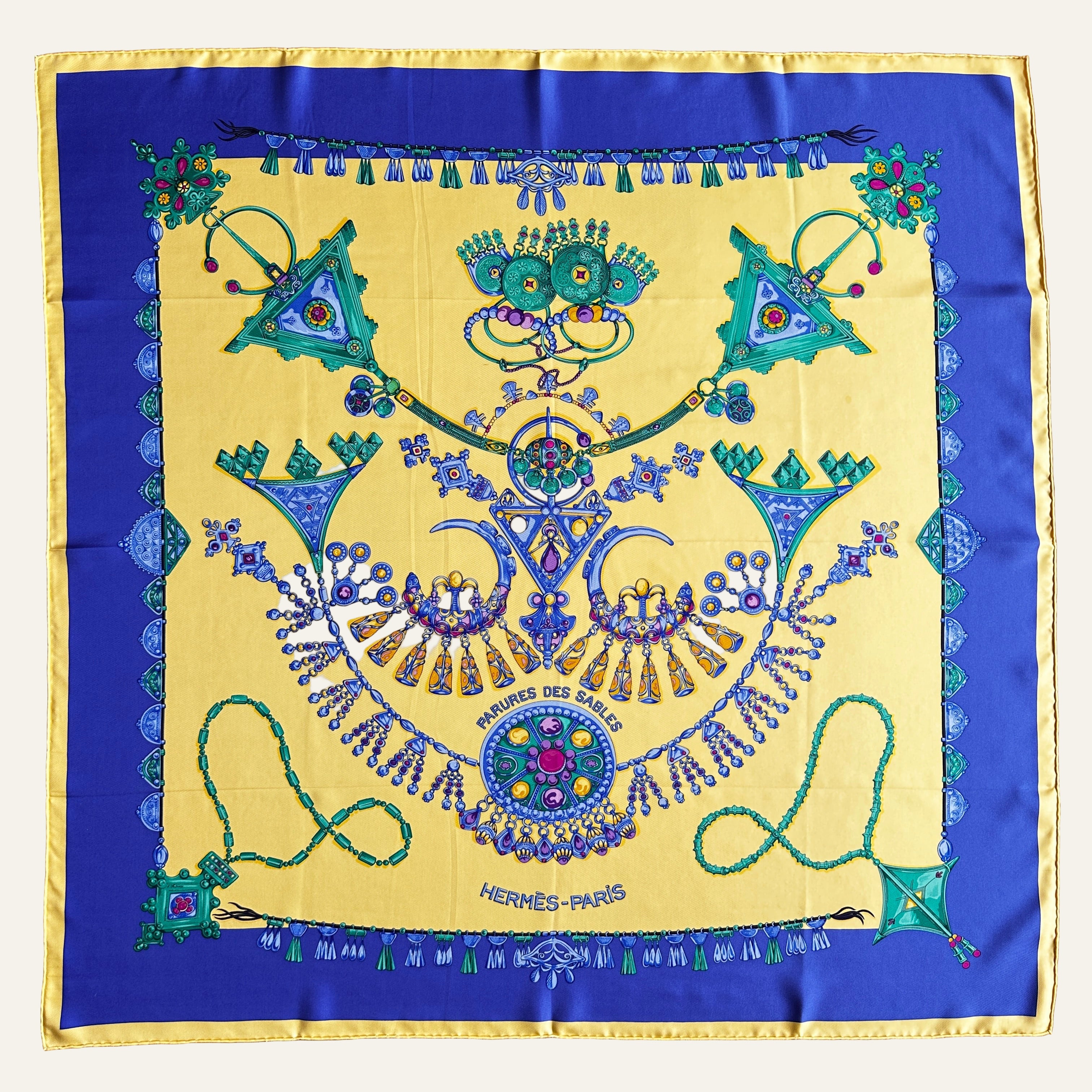 Foulard Hermès Parures des Sables bleu et jaune vue d'ensemble à plat, motifs de bijoux.