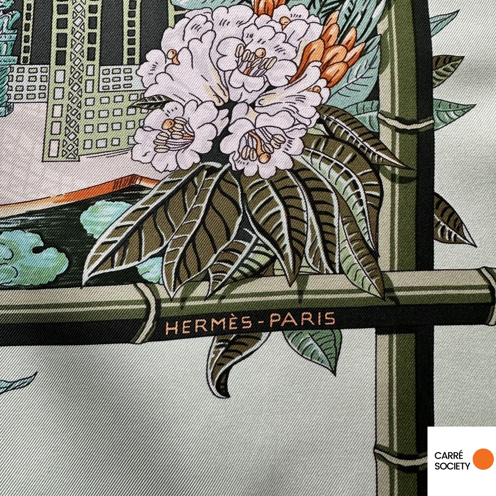 Gros plan sur le roulotté main du foulard Hermès Jardin d'Hiver et la signature HERMÈS PARIS.